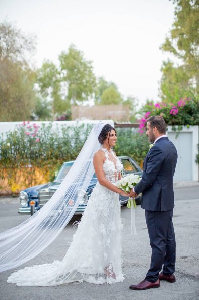 Bride and groom photograph pose looking at each other with the bridal bouquet in the middle of their embrace at a destination wedding in athenian riviera.