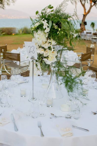 White simple wedding table setting with orchid flower centerpiece, crystal glasses, and silver cutlery for a destination wedding in athenian riviera.