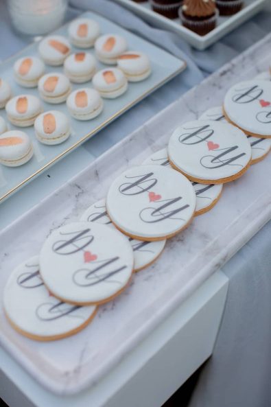 Custom made sugar cookies with sugar paste and couple's initials and rose gold brushed macarons for a wedding dessert table stand.