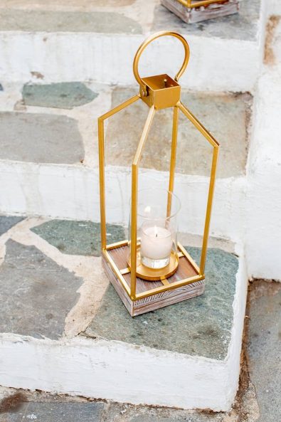 Minimal geometrical gold lantern with a white candle in a cobbled stone stair.