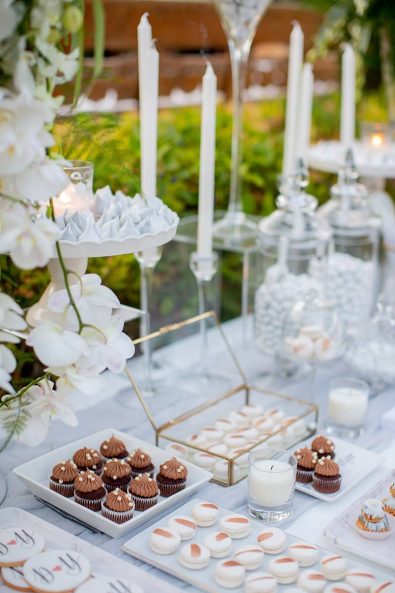 Close up shot of dessert station candy bar table with chocolate cupcakes, macarons, and sugar-coated almonds.