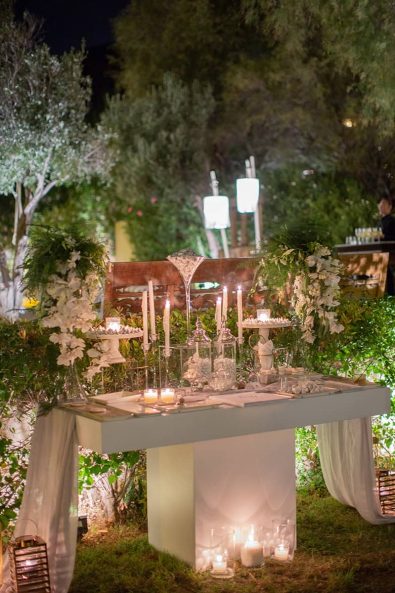 Night time shot of white and grey luxe wedding candy bar dessert table with lots of candles and sweets.
