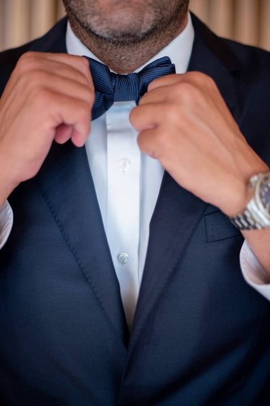 Close up shot of groom fixing his bow tie before his destination wedding in athenian riviera.