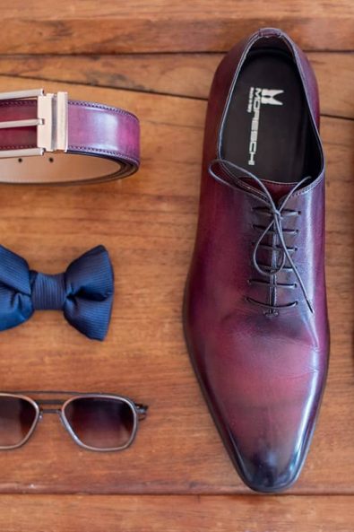 Flatlay shot of grooms shoes, bow tie, glasses, and belt.