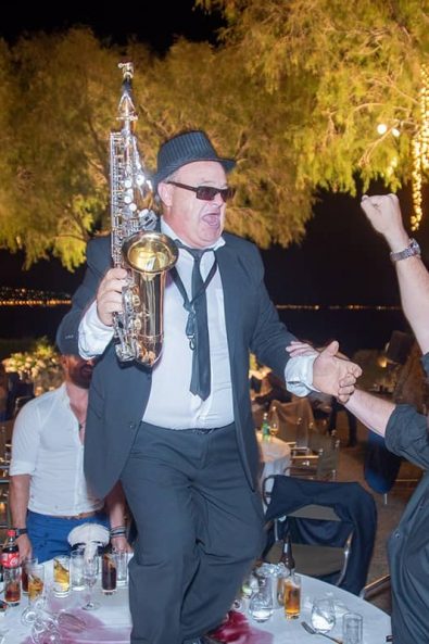 Folk artist with trumpet dancing on the table at a summer greek wedding.