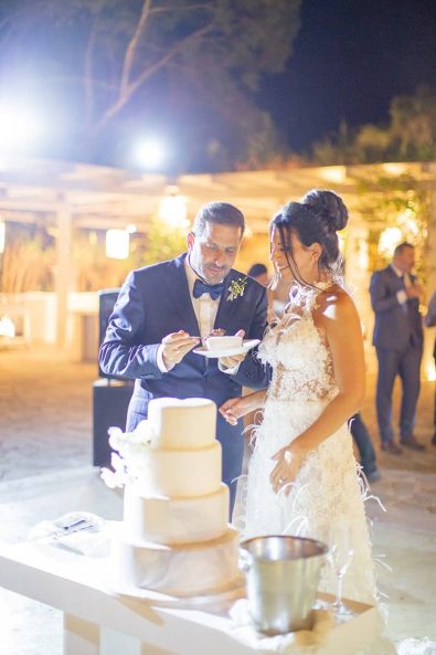 Bride and groom cutting their wedding cake feeding each other after their destination wedding in athenian riviera.