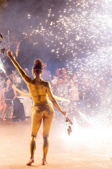 Fire acrobatics dancers with fireworks and fire instruments, gold bikinis and gold body painting for a wedding entertainment show at a destination wedding in athenian riviera .