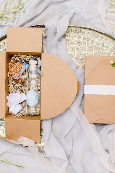 Wedding welcome guest gift in a craft box with raki aperitif, chocolate covered almonds and almond florentines and white seal wax stamp on the top.