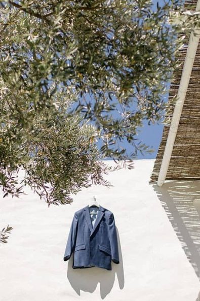 Shot of groom's navy blue suit hanging by a white wall.