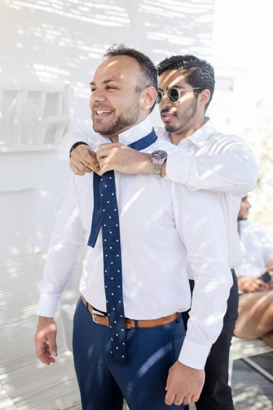 Best man tying the groom's tie on his preparation party before the wedding.