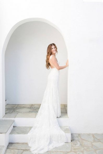 Island chic minimal bride with mermaid lace wedding dress with a white Aegean house in the background for a destination wedding in Greece.