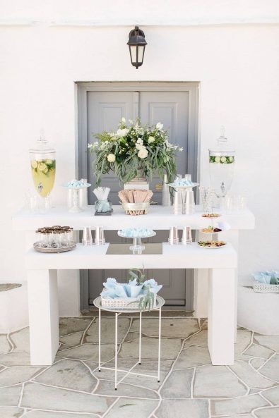 Refreshments stand with homemade lemonade and flavored water, glass and paper cups for serving, light blue details, and treats for guests to nibble on.