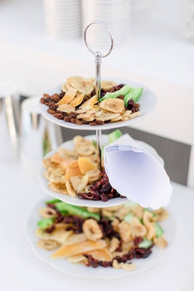 Triple tier serving tray with dried fruit, nuts and white paper cones for serving.