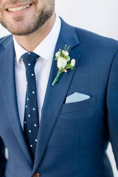 Close up shot of groom's lapel with a minimal white rose flower boutonniere.