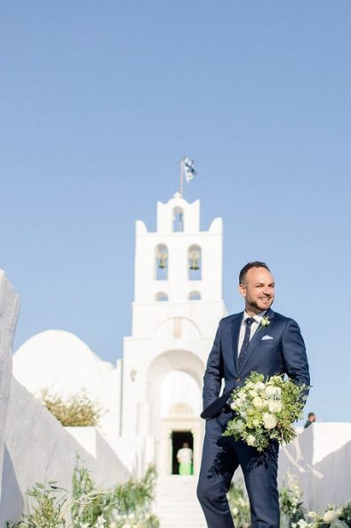 The groom in a navy blue suit and dotted necktie holding the bridal flowers waiting for his bride to arrive.