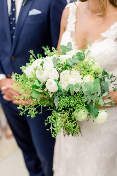 Close up shot of minimal and chic organic bridal bouquet with eucalyptus, white tulips, white peonies, white ranunculus and green wildflowers for a summer wedding.