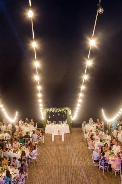 Wedding party with round tables, wooden floor, flower decorations, and fairy lights.