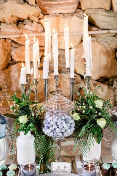 Close up shot of candy bar, dessert station with meringues in a glass serving bowl, flowers and greenery and cupcakes with blue frosting for a summer wedding.
