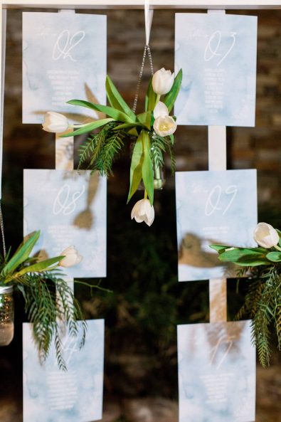 Dessert table backdrop with wedding stationary, tulips and greenery in glass jars.