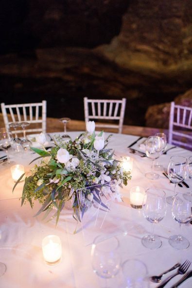 Clear table numbers and simple eucalyptus and white roses flower table centerpiece.