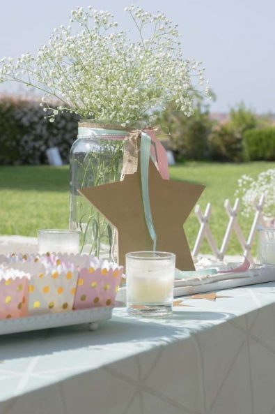 Greek orthodox baptism Christening party decorations with wooden stars and glass vases next to white and pink sweets boxes with gold polka dots.