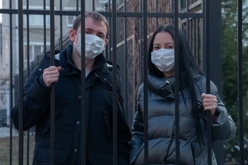 Man and woman wearing masks behind bars