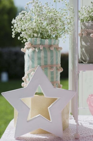 Pink star party decoration for baptism and flower arrangement with stripped fabric, pom poms and baby's breath.